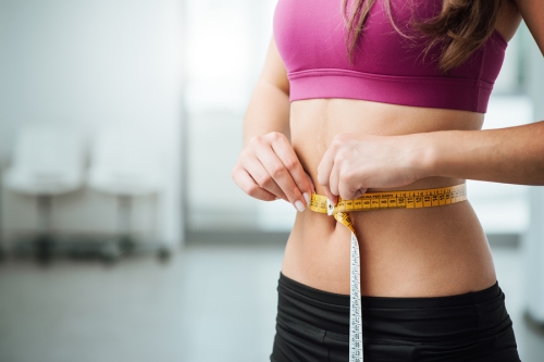 Slim young woman measuring her thin waist with a tape measure close up ** Note: Shallow depth of field